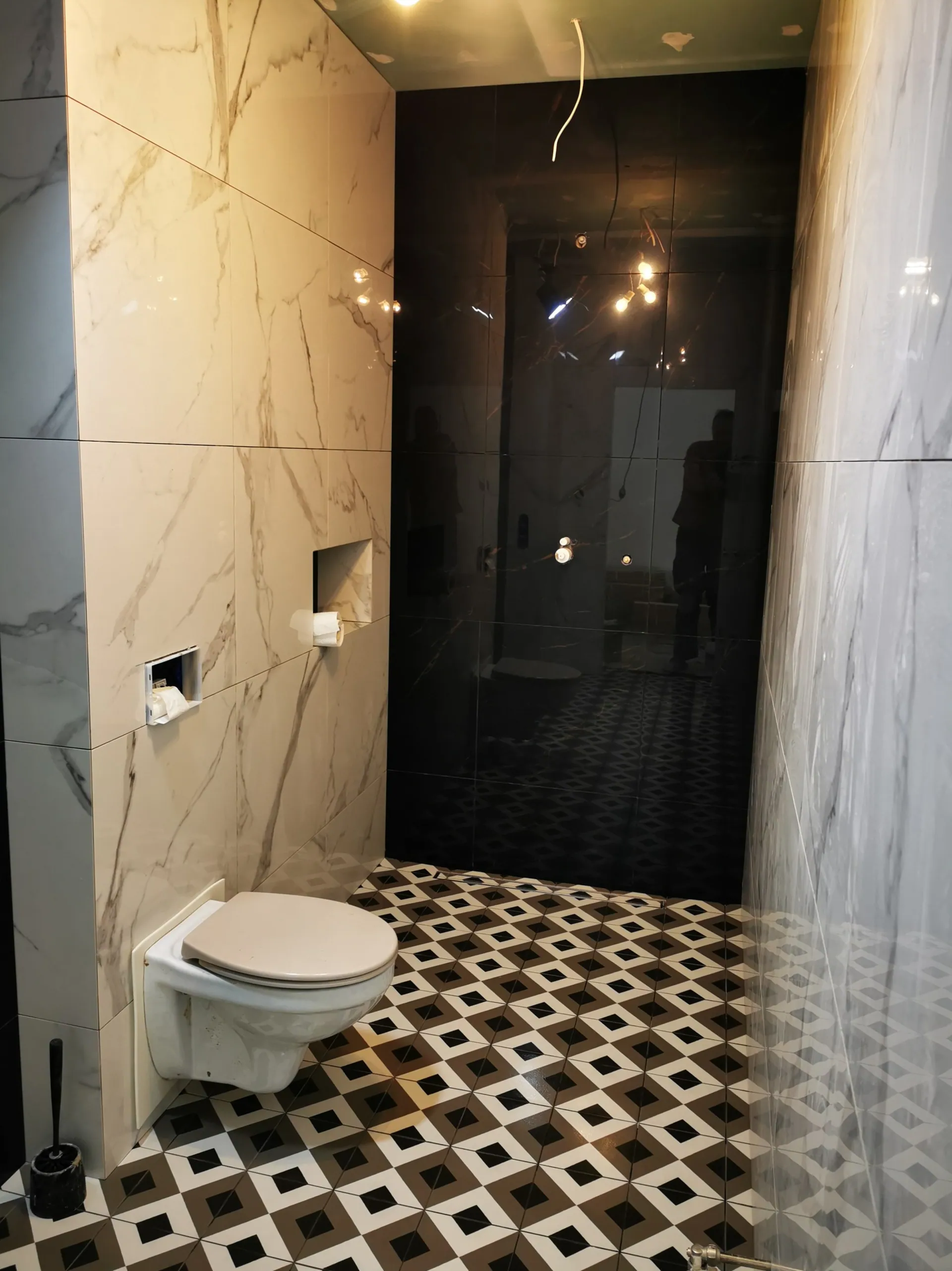 Efektowna łazienka z WC podwieszanym na ścianie z marmuru i czarną strefą prysznica z geometryczną podłogą.