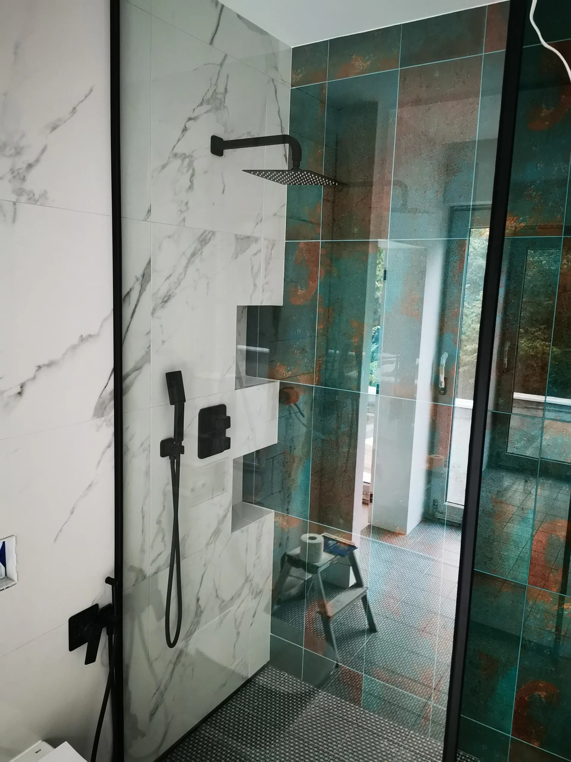 Szersze ujęcie kabiny walk-in z czarną armaturą, wnękami i mozaikową posadzką w brodziku.