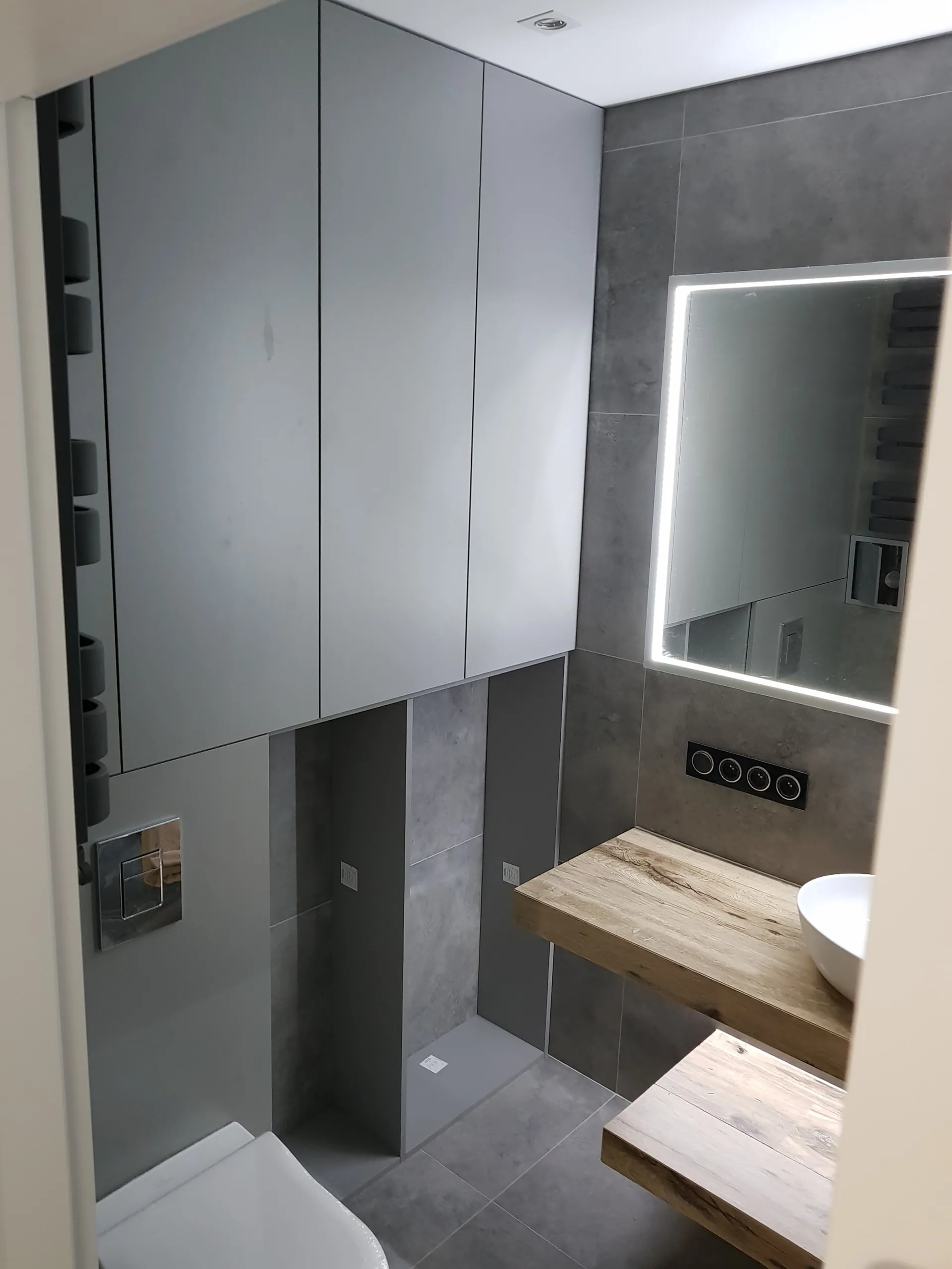 Zabudowa meblowa na całą wysokość nad WC, obok konsola z dębu i podświetlane lustro.